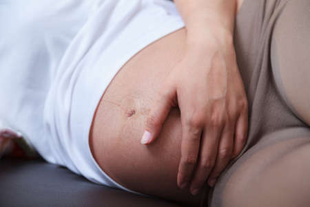Pregnant woman putting hand on the belly while sleeping on sofaの写真素材