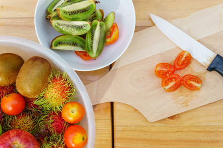 White knife with kiwi and tomato fruits on wooden floorの写真素材