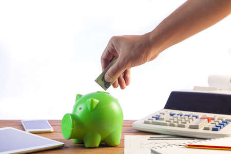Business man putting money coin into green piggy bank, finance and investment conceptの写真素材