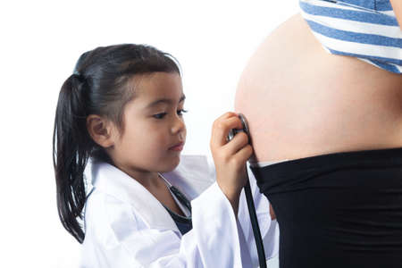 Little doctor listening with stethoscope for his unborn brother in his pregnant mothers bellyの写真素材