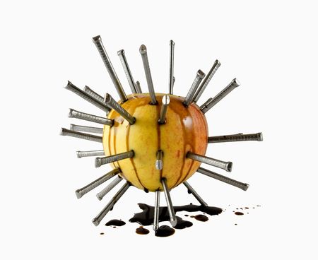 Many nails hammered into an apple leaking oil isolated on whiteの写真素材