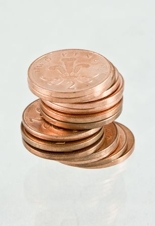 Unevenly stacked English two pence coins on a reflective base isolated on white