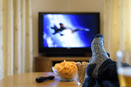 watching TV war movie (military jet) with feet on table, eating snacksの写真素材