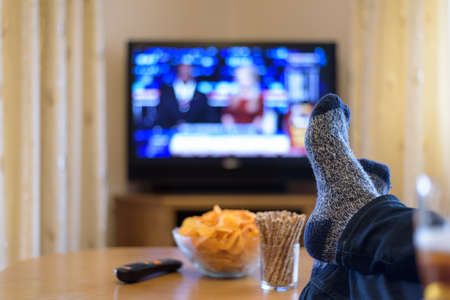 watching TV news with feet on table and eating snacksの写真素材