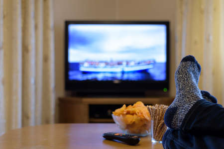 TV, television watching (boat with people) with feet on table eating snacks