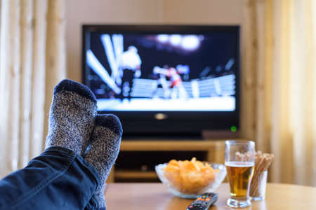 Television, TV watching (boxing match) with feet on table eating snacks and drinking beer - stock photoの写真素材