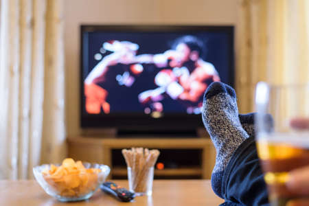 Television, TV watching (boxing match) with feet on table eating snacks and drinking beer - stock photoの写真素材