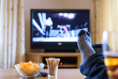 Television, TV watching (boxing match) with feet on table eating snacks and drinking beer - stock photoの写真素材