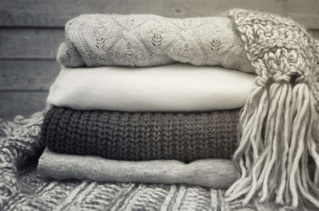 Knitted sweaters and fallen yellow leaves on a wooden background
