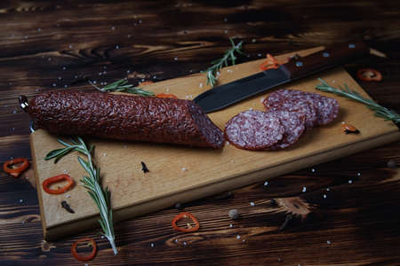 Smoked sausage on a wooden cutting board with a scattering of spicesの写真素材