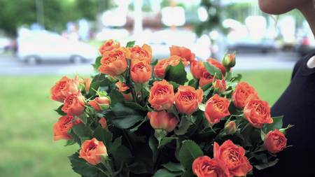 Girl enjoys a bouquet of orange roses in the cityの写真素材