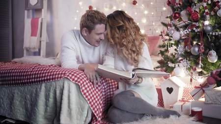 Young beautiful looking at photo album on bed near christmas treeの写真素材