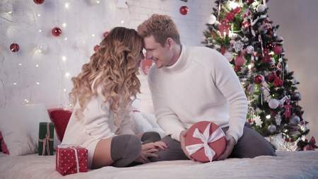 Young beautiful woman gives a Christmas gift to a man near a Christmas treeの写真素材