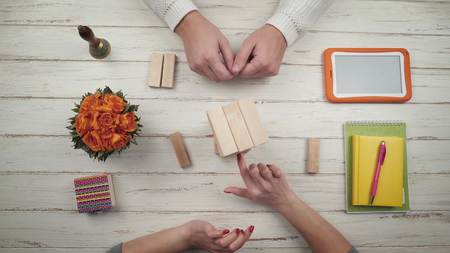 A couple playing a board game janga on a stylish white wooden table. Nearby there are flowers and a digital tablet. Top view. Hands close up viewの写真素材