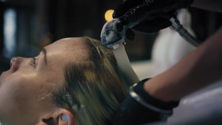 Hairdresser in black gloves carefully washes females hair with conditioner in sink in hair salon, and then turns off the water. Closeupの写真素材