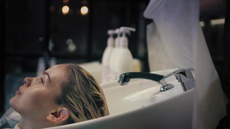 Hairdresser softly wraps womans long blonde hair in a towel in sink after washing. Profile angle.