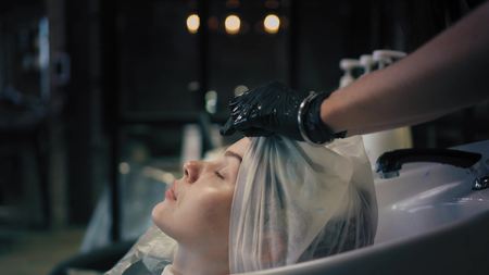 Hairdresser softly wraps womans long blonde hair in a towel in sink after washing. Profile angle.
