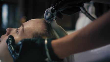 Hairdresser in black gloves carefully washes females hair with conditioner in sink in hair salon, and then turns off the water. Closeupの写真素材