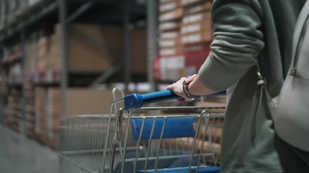 Closeup view on woman in a store with a shopping trolley. Hands are on a shopping cart. Woman is...