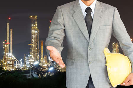 businessman with handshake to cooperation and oil refinery night backgroundの写真素材