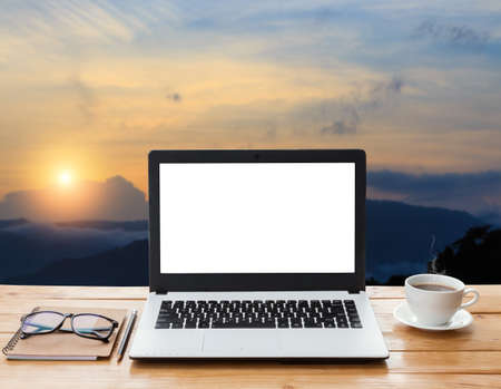 laptop computer and coffee on wood workspace and mountain at sunset backgroundの写真素材