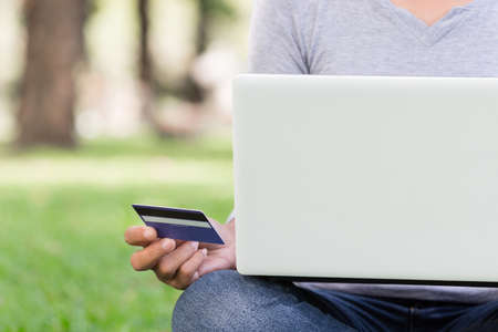 woman using laptop and credit card shopping online in parkの写真素材