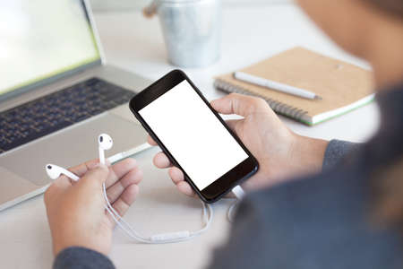 woman holding headphone and phone white screen on table third person view