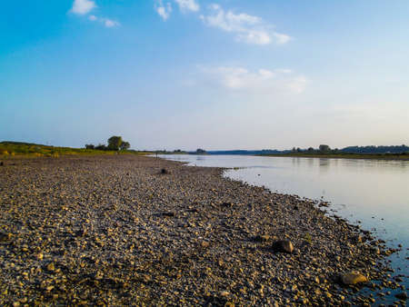 Rocky shore of a broad river, the reflection of clouds in waterの写真素材