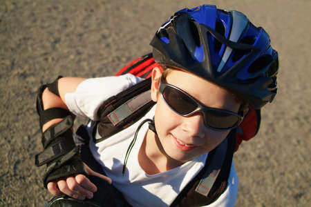 A nine year old boy wearing sunglasses, a bike helmet and a backpack crouches in a sunny park.の写真素材