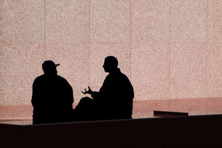 Two men having an animated conversation are silhouetted against a pink stone wall.の写真素材