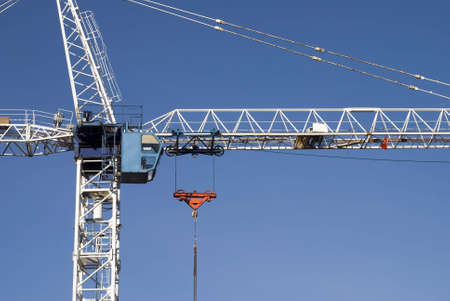 A white construction crane stands against a clear blue sky.