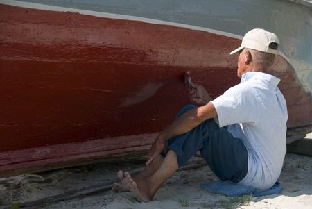 A man slowly painting the hull of an old boat.の写真素材