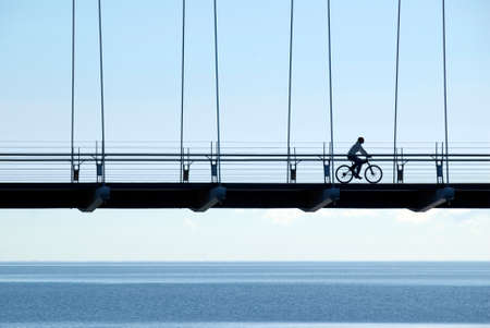 A woman riding a mountain bike across a suspension bridge near Lake Ontario, just after dawn.の写真素材