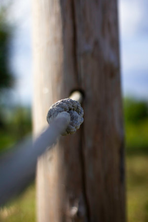 A rope is tied to a wooden post. The rope is white and has a gray tinge