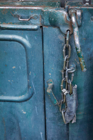 A chain is hanging from a lock on a blue object. The chain is rusty and the lock is brokenの写真素材
