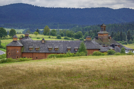 A large wooden building with a lot of windows sits in a field. The building is surrounded by trees and the sky is cloudyの写真素材