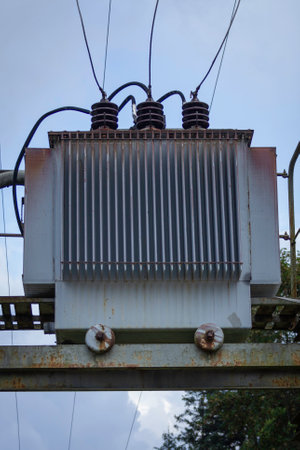 A large power station with three tall poles and a large white box on top. The box is surrounded by many wires and is surrounded by a rusted metal frame. The sky is clear and the sun is shiningの写真素材