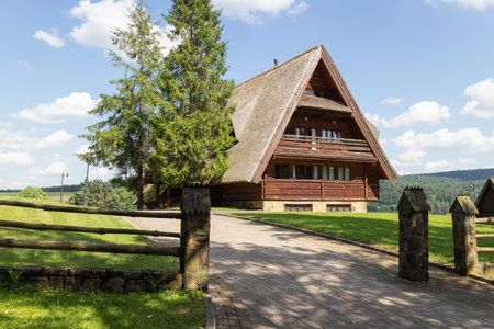 A small house with a wooden roof sits on a grassy hill. The house is surrounded by a wooden fence and has a driveway leading up to it. The house appears to be a cozy, rustic cabin with a warmの写真素材