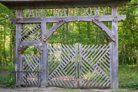 A wooden gate with a sign that says Parka. The gate is open and has a bench attached to it. The gate is surrounded by trees and is in a forestの写真素材