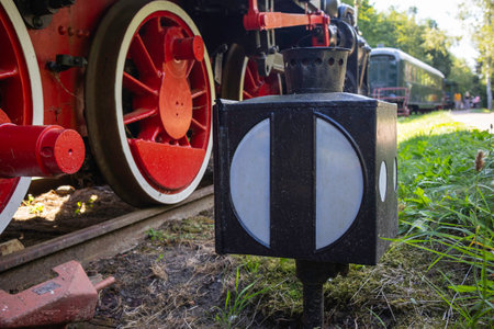 A train with a red and black wheel and a black and white box on the ground. The box has a white light insideの写真素材