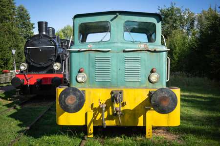 A green train with yellow trim sits next to a black train. The green train is old and rustyの写真素材
