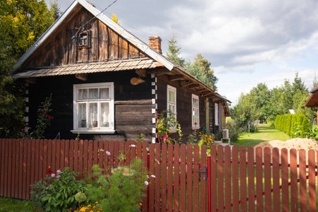 A small house with a red fence and a white door. The house is surrounded by a garden with flowers and plantsの写真素材