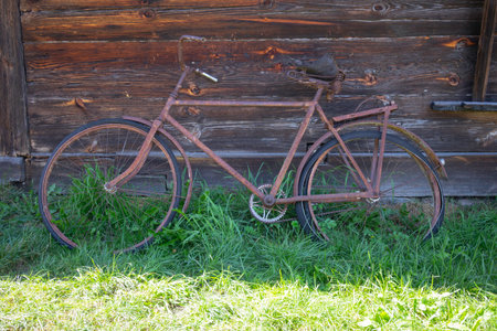 An old bicycle is leaning against a wooden fence. The bike is rusty and has a wooden seat. The bike is in a grassy area, and the fence is made of wood. The scene gives off a nostalgic and rustic vibeの写真素材