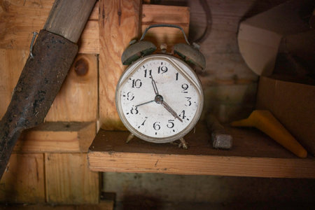 A white alarm clock with the hands on the number 3 and 6. The clock is on a wooden shelfの写真素材