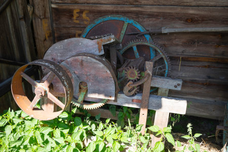 An old machine with a green gear sits in a field of weeds. The machine is rusty and has a wooden frame. The scene is quiet and peaceful, with the machine being the only thing in focusの写真素材