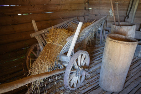 A wooden cart filled with hay is sitting in the middle of a barn. The hay is piled up on the cart, creating a cozy and rustic atmosphere. The barn itself is made of wood and has a warmの写真素材