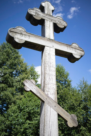 A wooden cross with three arms and a cross on top. The cross is leaning on a tree trunkの写真素材