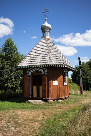 A small wooden building with a pointed roof and a cross on top. The building is surrounded by trees and grassの写真素材