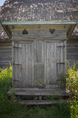 A wooden outhouse with a roof and a door with a heart on it. The door is open and the inside is emptyの写真素材