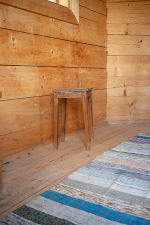 A wooden stool sits in front of a wooden wall. The stool is old and worn, and the wall is made of wood. The room is small and cozy, with a rug on the floorの写真素材